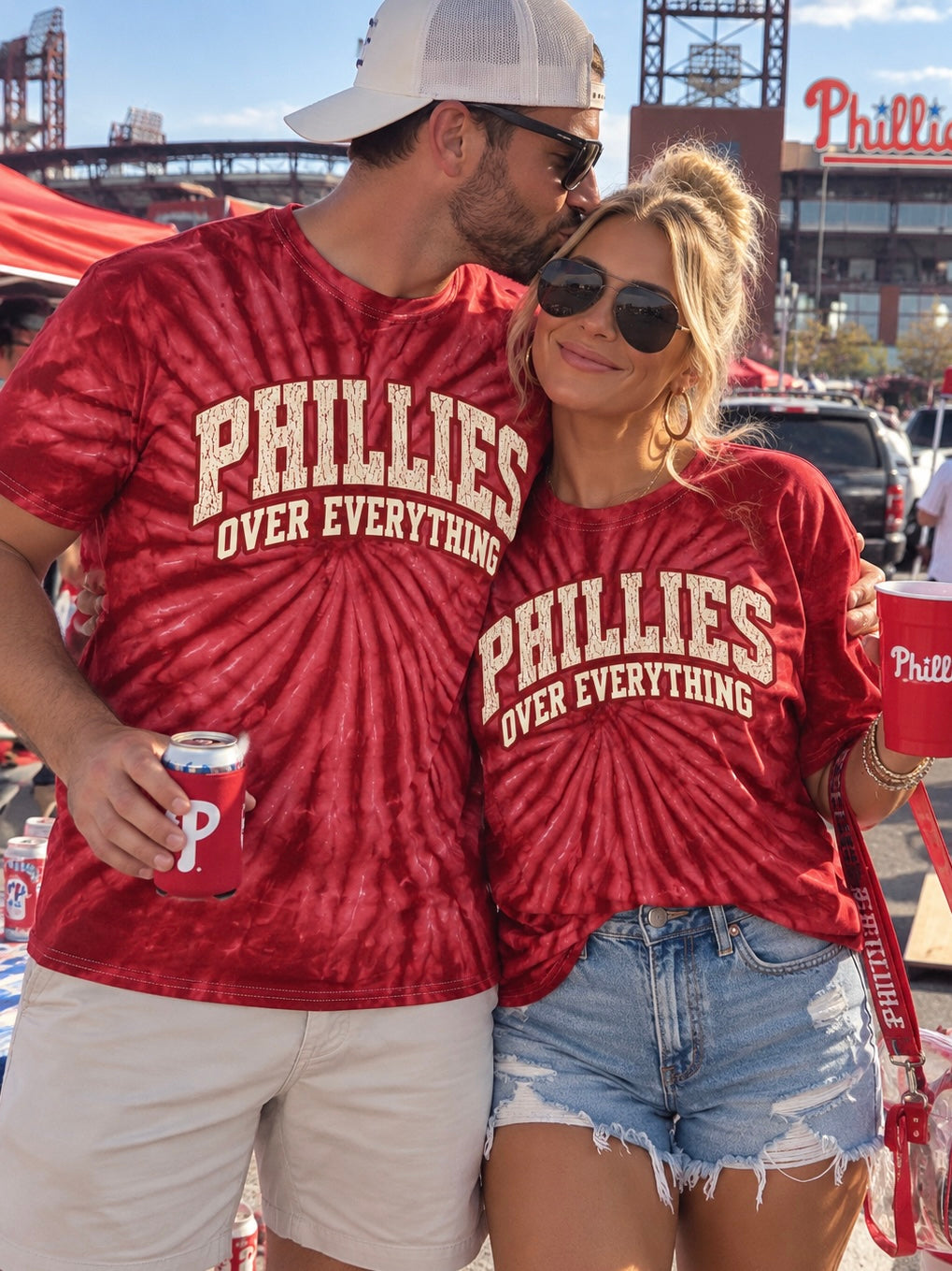 A man and a woman standing together at a Philadelphia Phillies event, both wearing matching red tie-dye t-shirts with 'PHILLIES OVER EVERYTHING' printed in cream across the chest.